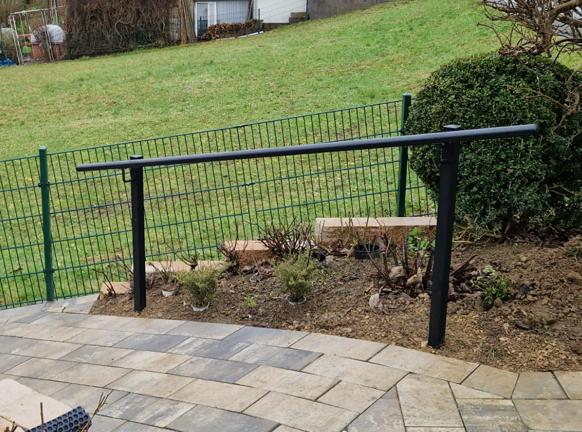 Schwarzer Handlauf entlang eines Gartenwegs